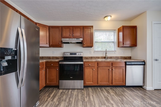 kitchen with appliances with stainless steel finishes, a sink, under cabinet range hood, and wood finished floors