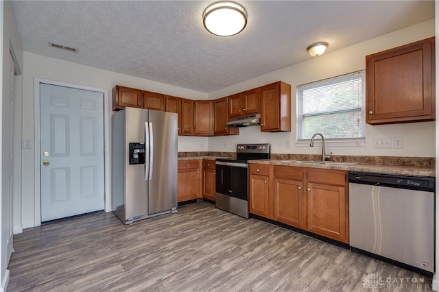 kitchen featuring stainless steel appliances, brown cabinets, a sink, and under cabinet range hood