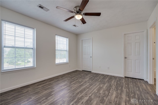 unfurnished room with a textured ceiling, a wealth of natural light, dark wood-style flooring, and visible vents