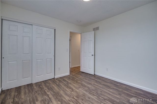 unfurnished bedroom with a textured ceiling, wood finished floors, visible vents, baseboards, and a closet