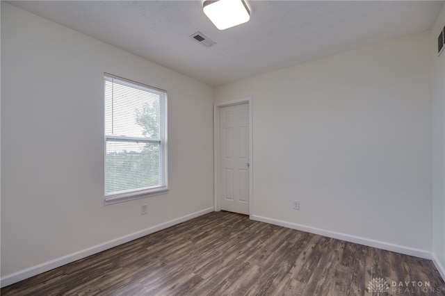 spare room with baseboards, visible vents, and dark wood-style flooring