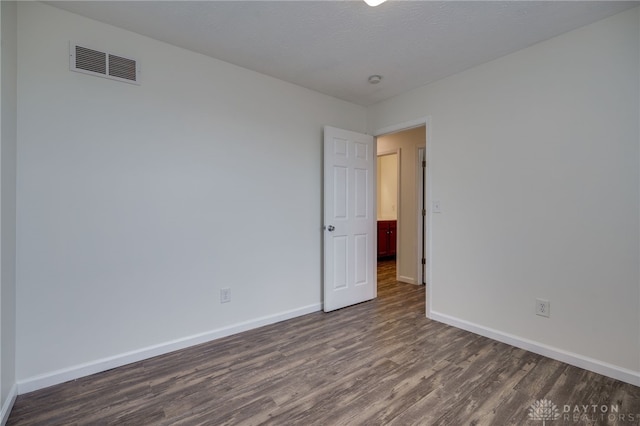 empty room with dark wood-style flooring, visible vents, a textured ceiling, and baseboards