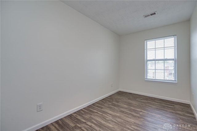 spare room with a textured ceiling, dark wood-style flooring, visible vents, and baseboards