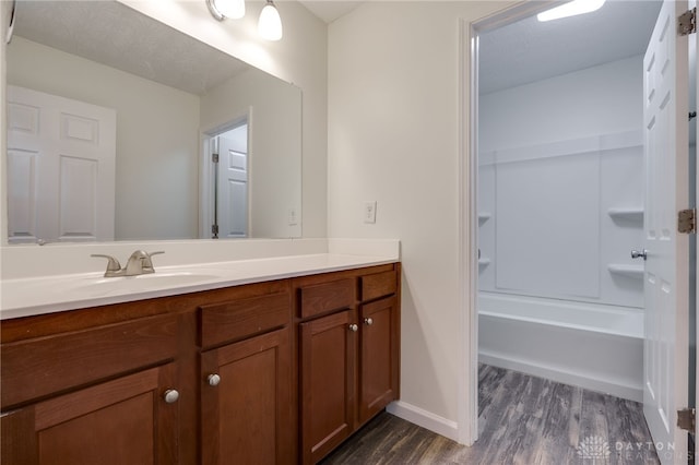 bathroom featuring baseboards, wood finished floors, a textured ceiling, vanity, and shower / bathing tub combination