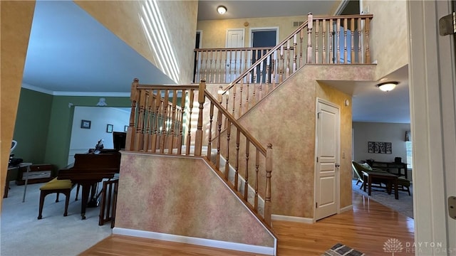 stairway with baseboards, crown molding, a high ceiling, and wood finished floors