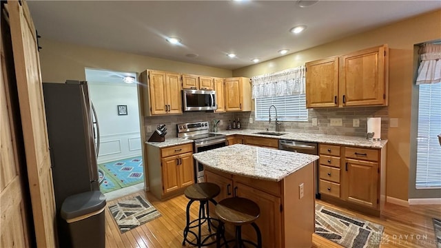 kitchen featuring a center island, backsplash, appliances with stainless steel finishes, a sink, and light wood-type flooring