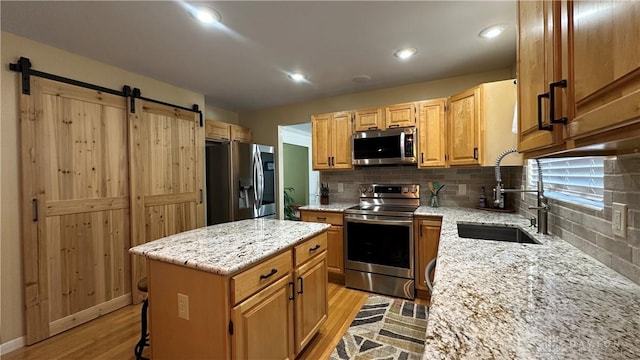 kitchen featuring light wood finished floors, backsplash, a barn door, appliances with stainless steel finishes, and a sink