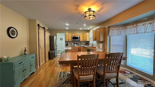 dining room with a barn door, baseboards, and light wood-style flooring