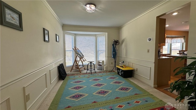 rec room featuring crown molding, wainscoting, light colored carpet, and a decorative wall