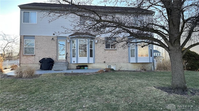 rear view of house featuring entry steps, fence, a lawn, and brick siding