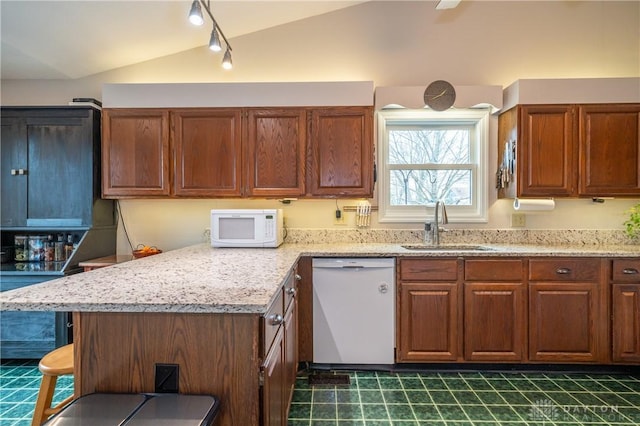 kitchen with lofted ceiling, a peninsula, white appliances, a sink, and brown cabinets