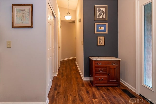 hall with dark wood-style flooring, visible vents, and baseboards