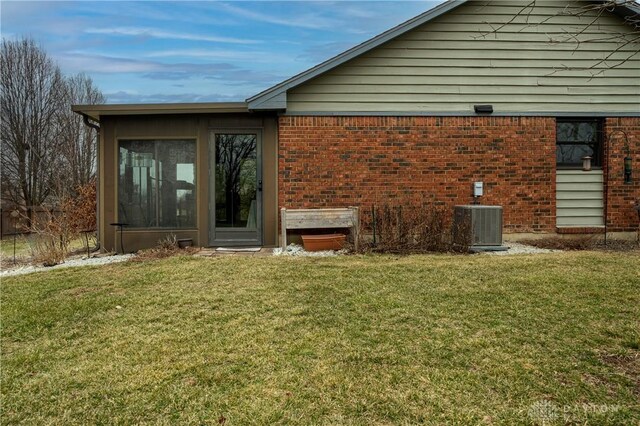 rear view of house featuring a sunroom, central AC, a lawn, and brick siding