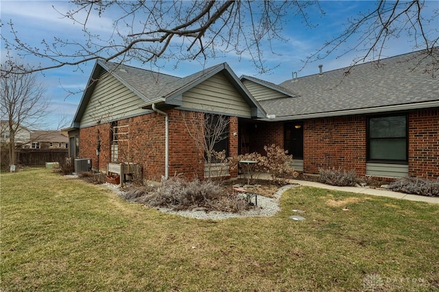 exterior space with roof with shingles, brick siding, a front lawn, and central air condition unit