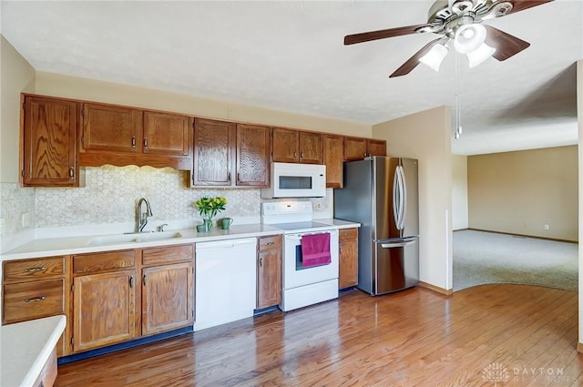 kitchen featuring light countertops, backsplash, a sink, wood finished floors, and white appliances