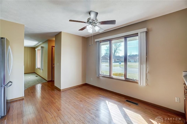 spare room featuring ceiling fan, light wood-style flooring, visible vents, and baseboards