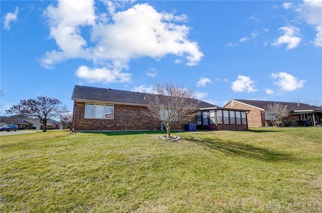 view of front of home featuring a sunroom, a front lawn, and brick siding