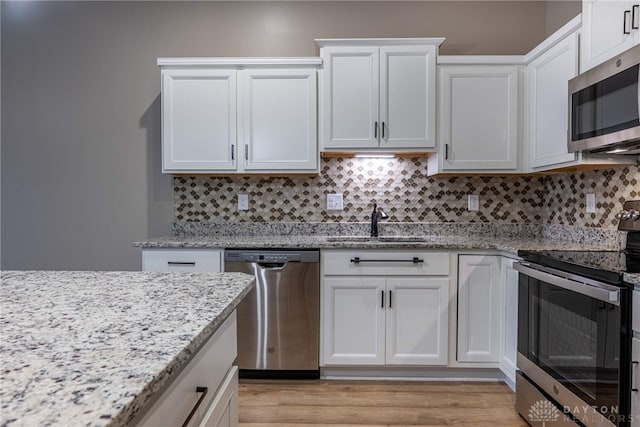 kitchen featuring white cabinets, decorative backsplash, light stone counters, stainless steel appliances, and a sink