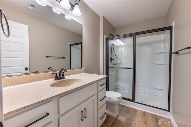 bathroom featuring visible vents, toilet, wood finished floors, vanity, and a shower stall