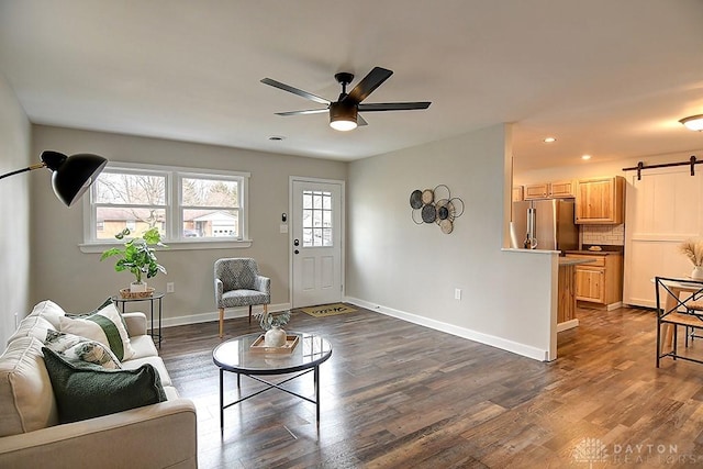 living area featuring a barn door, dark wood finished floors, a ceiling fan, and baseboards