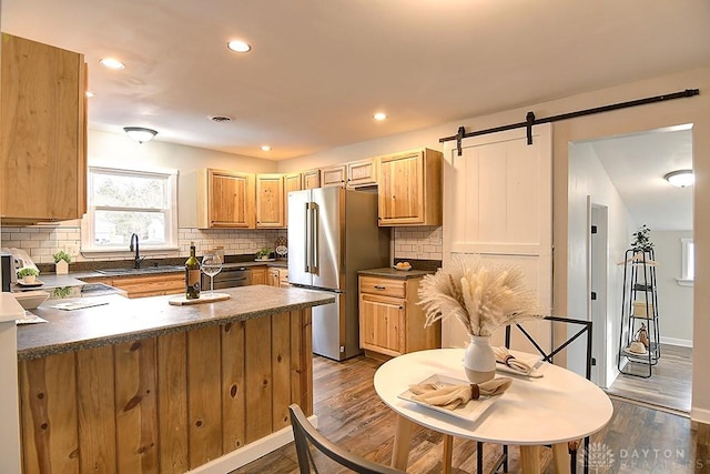 kitchen with a barn door, dark countertops, dark wood-style floors, freestanding refrigerator, and a sink