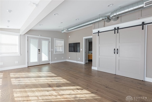 unfurnished living room featuring french doors, visible vents, a barn door, wood finished floors, and baseboards