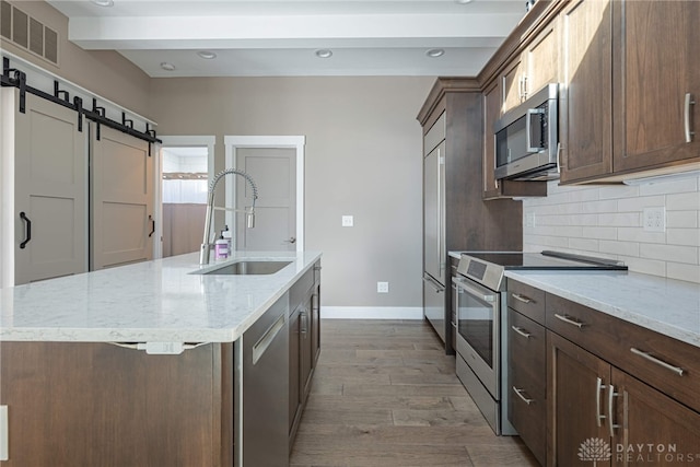 kitchen featuring a barn door, stainless steel appliances, a sink, visible vents, and tasteful backsplash