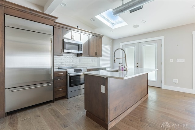 kitchen with lofted ceiling with skylight, light wood-style flooring, a sink, stainless steel appliances, and backsplash