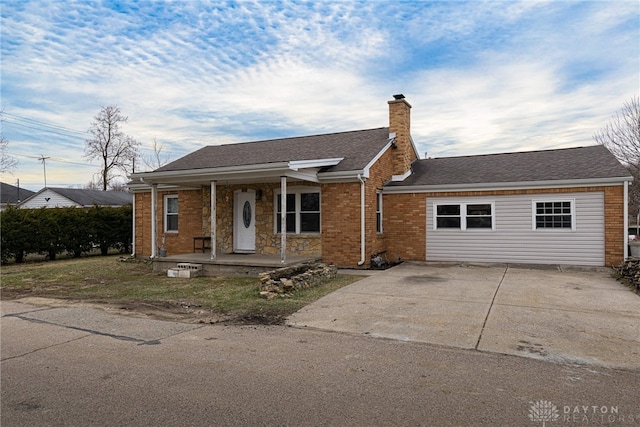 view of front of property with brick siding, roof with shingles, a chimney, a porch, and driveway