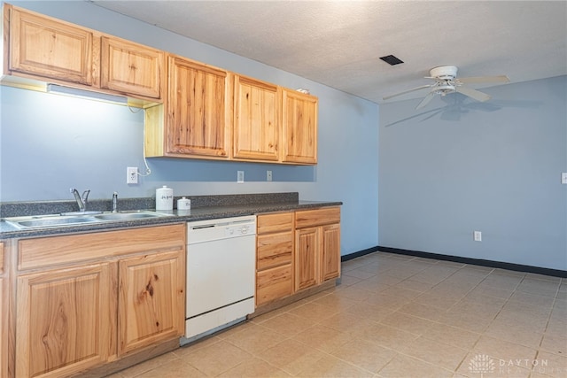 kitchen with light brown cabinetry, white dishwasher, dark countertops, a sink, and a ceiling fan