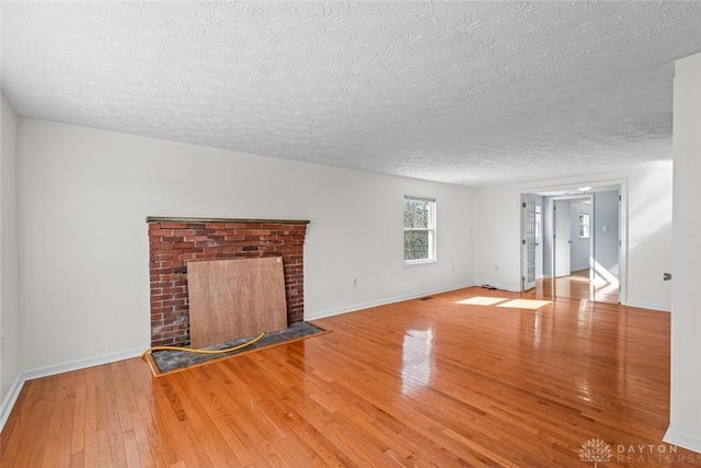 unfurnished living room with a brick fireplace, a textured ceiling, baseboards, and hardwood / wood-style flooring