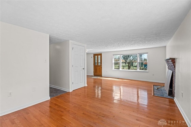 unfurnished living room with a textured ceiling, wood finished floors, a fireplace with flush hearth, and baseboards