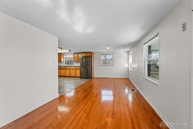 unfurnished living room with light wood-style floors, baseboards, visible vents, and a textured ceiling