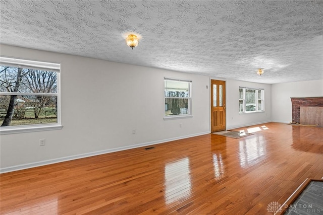 unfurnished living room featuring a fireplace, a textured ceiling, baseboards, and hardwood / wood-style flooring