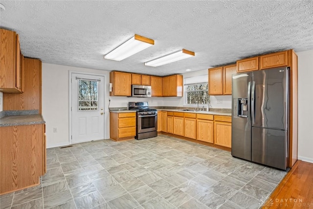 kitchen featuring appliances with stainless steel finishes, brown cabinetry, a sink, and baseboards