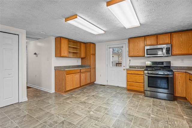 kitchen featuring baseboards, appliances with stainless steel finishes, brown cabinets, a textured ceiling, and open shelves