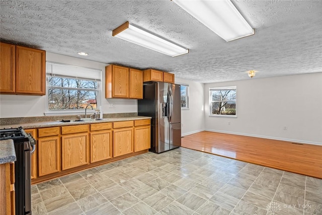 kitchen with brown cabinets, a sink, gas range, stainless steel fridge, and baseboards