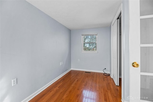 unfurnished bedroom with wood-type flooring, visible vents, baseboards, and a closet