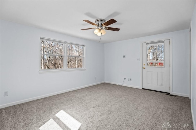 carpeted spare room with baseboards, visible vents, a ceiling fan, and a healthy amount of sunlight