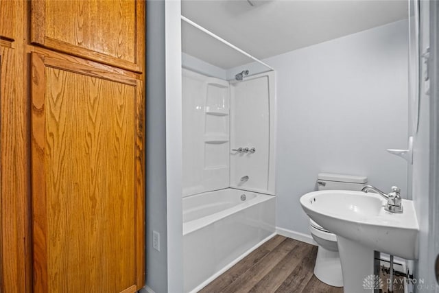 bathroom with toilet, baseboards,  shower combination, and wood finished floors