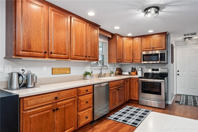 kitchen with brown cabinets, dark wood finished floors, visible vents, appliances with stainless steel finishes, and a sink