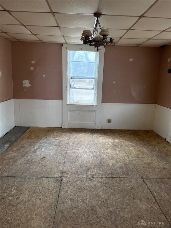 unfurnished dining area featuring a wainscoted wall, a drop ceiling, and an inviting chandelier