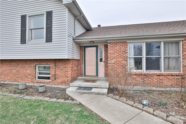 doorway to property featuring brick siding and a shingled roof