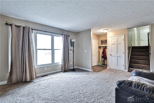 living area featuring carpet floors, stairway, baseboards, and a textured ceiling