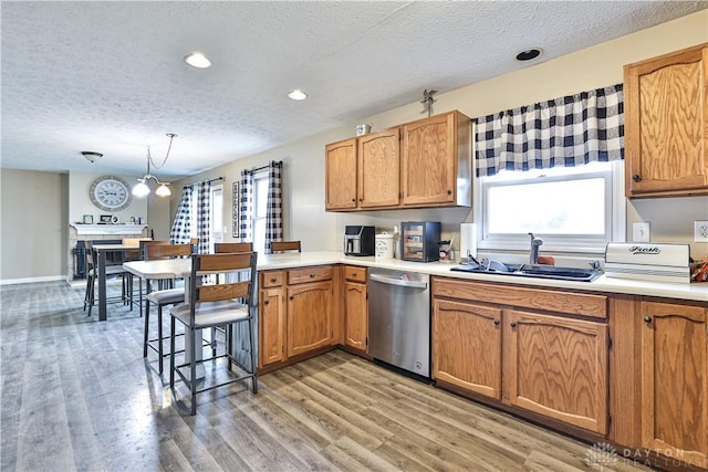 kitchen featuring light wood-style flooring, a peninsula, a sink, light countertops, and stainless steel dishwasher