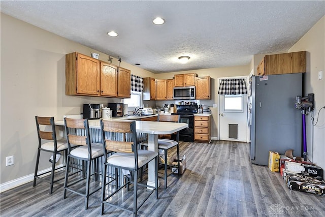 kitchen with appliances with stainless steel finishes, brown cabinetry, a sink, wood finished floors, and a peninsula