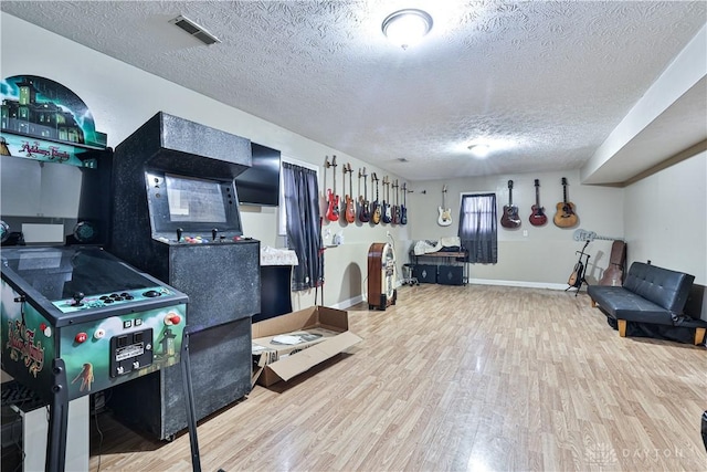 rec room with baseboards, a textured ceiling, visible vents, and wood finished floors