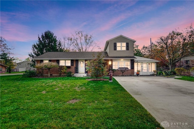 view of front of house featuring concrete driveway, brick siding, fence, and a front lawn