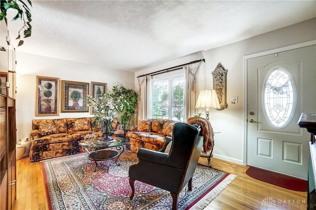 living area featuring a textured ceiling, light wood-style flooring, and baseboards