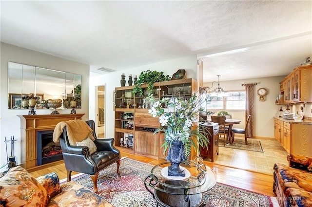 living room featuring light wood finished floors, a fireplace, visible vents, and a notable chandelier